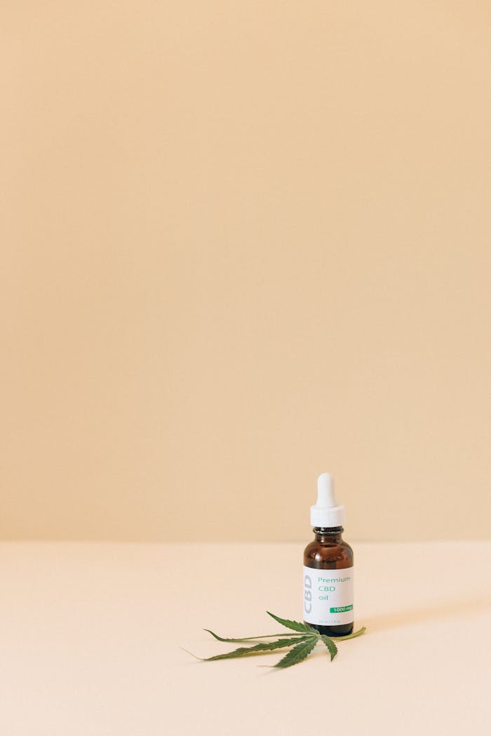 Minimalist image of a CBD oil bottle with a cannabis leaf on beige background.